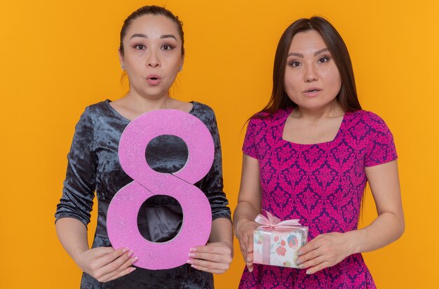 Kostenloses Foto zwei glückliche und überraschte asiatische frauen feiern den internationalen frauentag mit der nummer acht