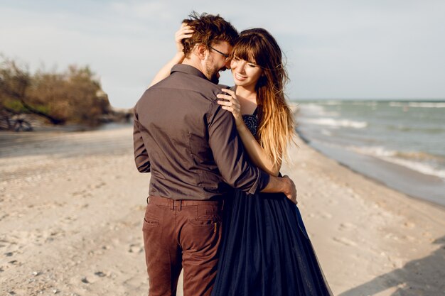 Zwei glückliche verliebte, elegante Frau mit ihrem hübschen Freund, der romantische Zeit zusammen am Strand umarmt und genießt. Elegantes Kleid.