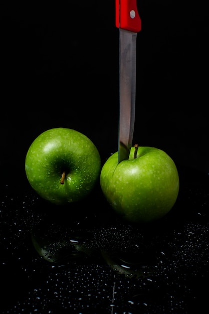 Kostenloses Foto zwei grüne äpfel mit einem messer auf einem schwarzen