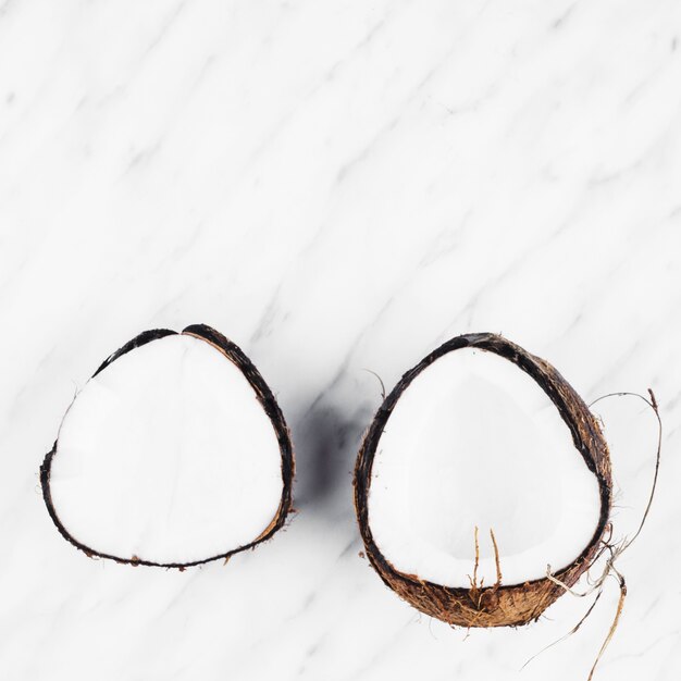 Zwei Hälften der reifen Kokosnuss auf weißem Marmor Hintergrund