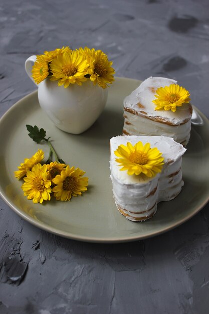 Zwei Herzformhonigkuchen mit Dekor von den gelben Blumen auf keramischer Platte