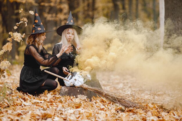 Zwei Hexenmädchen im Wald an Halloween. Mädchen, die schwarze Kleider und Kegelhüte tragen. Hexen machen einen Zaubertrank.