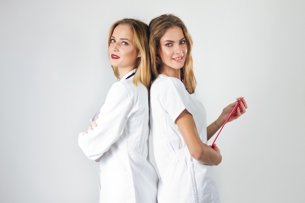 Zwei hübsche junge Frauen Ärzte, Krankenschwestern stehen zurück zu Rücken in das Krankenhaus.