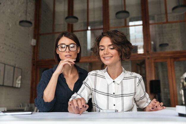 Zwei hübsche lächelnde Schönheitsfrauen, die am Tisch sitzen