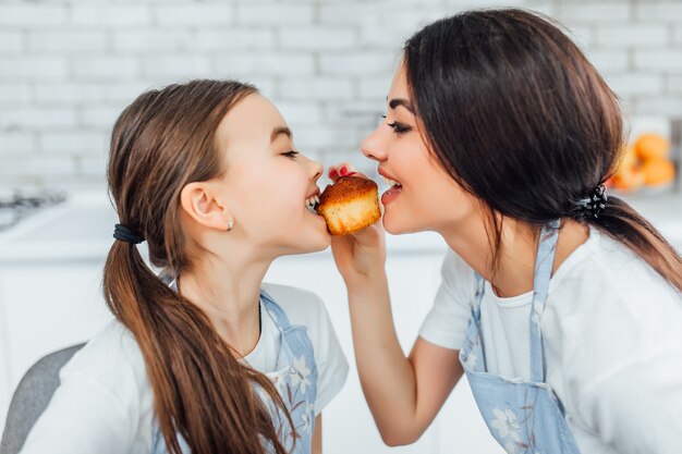 Zwei hübsche Mädchen probieren Cupcakes in der Küche