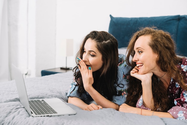 Zwei junge Frauen, die auf dem Bett betrachtet Laptopbildschirm liegen