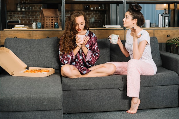 Zwei junge Frauen, die auf dem Sofa frühstückt sitzen
