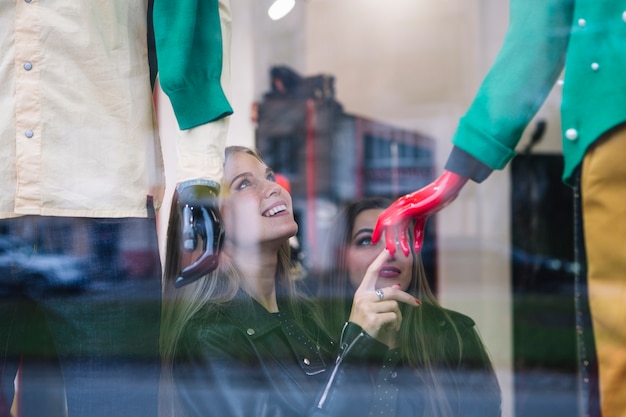 Zwei junge Frauen, die das Fenstereinkaufen vor Butikenspeicherausstellungsfenster tun
