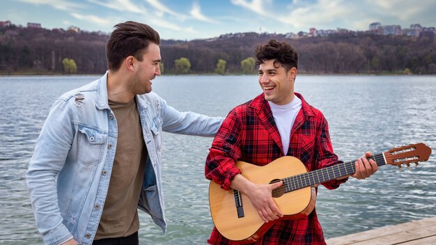 Zwei junge Freunde singen und spielen Gitarre in der Nähe eines Sees in einem Park