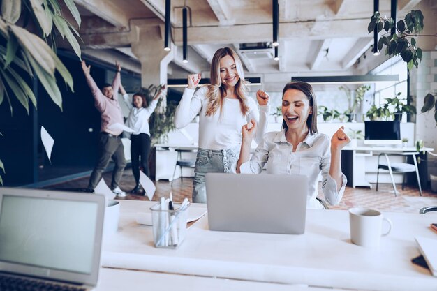 Zwei junge glückliche Geschäftsfrauen, die Projekterfolg im Büro feiern