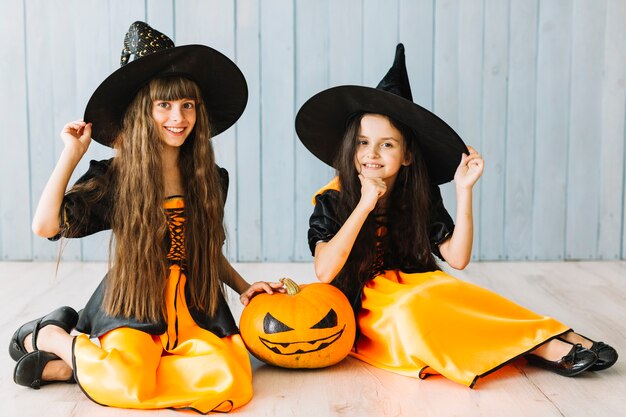 Zwei junge Hexen, die auf Fußboden auf Halloween lächeln und sitzen