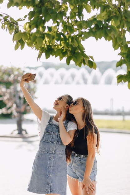 Zwei junge hübsche Mädchen auf einem Spaziergang im Park, die am Telefon Fotos von sich machen