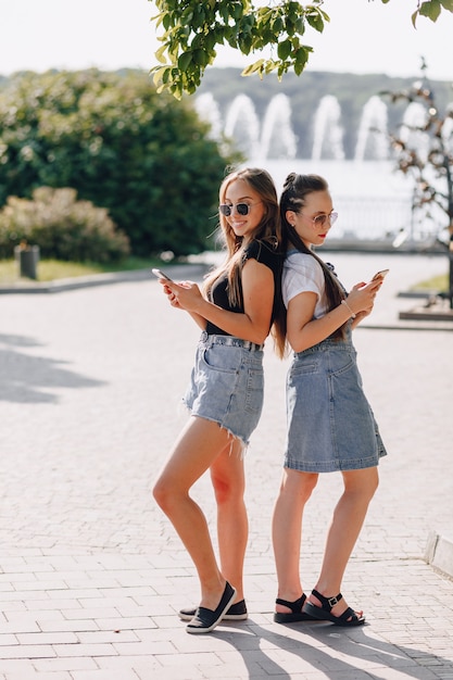 Zwei junge hübsche Mädchen auf einem Spaziergang im Park mit Telefonen. sonniger Sommertag, Freude und Freundschaften.