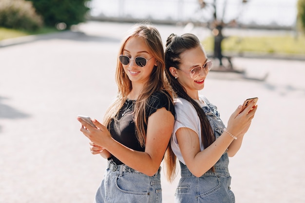 Zwei junge hübsche Mädchen auf einem Spaziergang im Park mit Telefonen