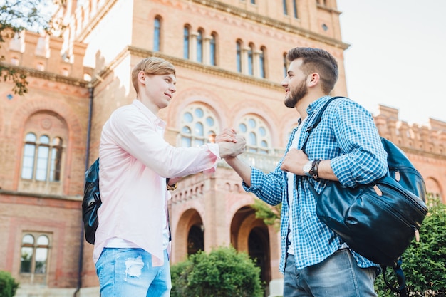 Zwei junge hübsche Studenten mit Rucksäcken begrüßen sich auf dem Campus. in der Universität.