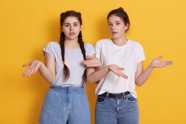 Zwei junge junge Frauen im Teenageralter in weißen T-Shirts, die mit sich ausbreitenden Händen posieren