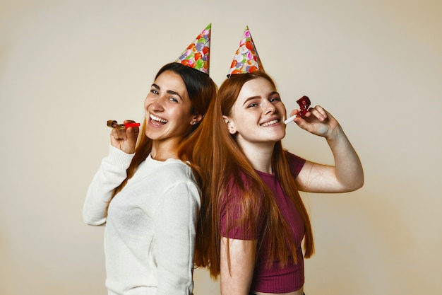 Zwei junge kaukasische Mädchen in den Geburtstagshüten lächeln aufrichtig