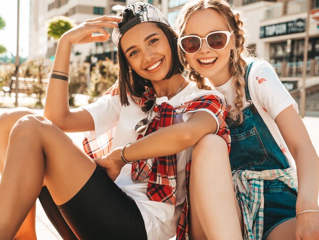 Zwei junge lächelnde schöne Mädchen mit bunten Penny Skateboards. Frauen im Sommer Hipster Kleidung sitzen im Straßenhintergrund. Positive Models, die Spaß haben und verrückt werden