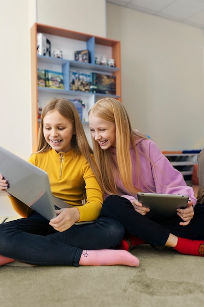 Zwei junge Mädchen, die mit ihrem Laptop und Tablet zusammenarbeiten