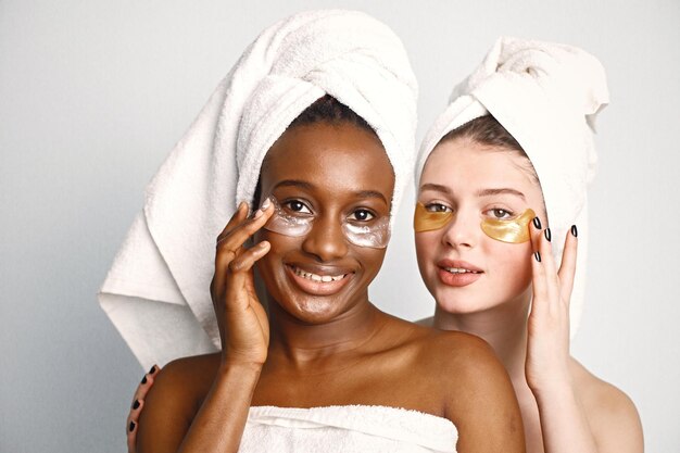Zwei junge Mädchen im Teenageralter mit Augenflecken im Gesicht haben ein in Handtücher gewickeltes Haar