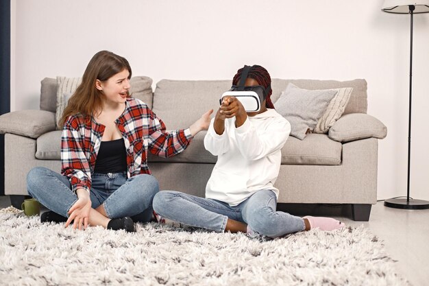 Zwei junge Mädchen im Teenageralter sitzen auf einem Boden neben dem Bett und tragen eine Virtual-Reality-Brille