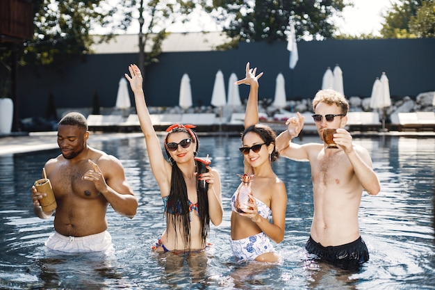 Zwei junge Mädchen und zwei ihre männlichen Freunde, die sich im Schwimmbad entspannen. Mädchen, die blaue und rote Badebekleidung tragen.