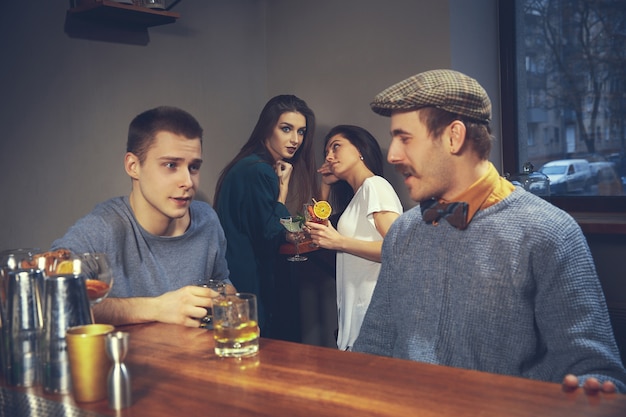 Zwei junge männer in freizeitkleidung sprechen beim sitzen am bartheke in der kneipe