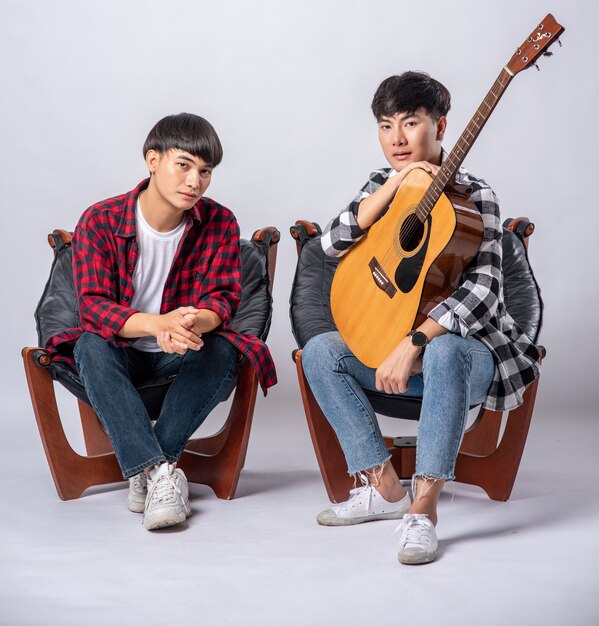 Zwei junge Männer sitzen auf einem Stuhl und halten eine Gitarre