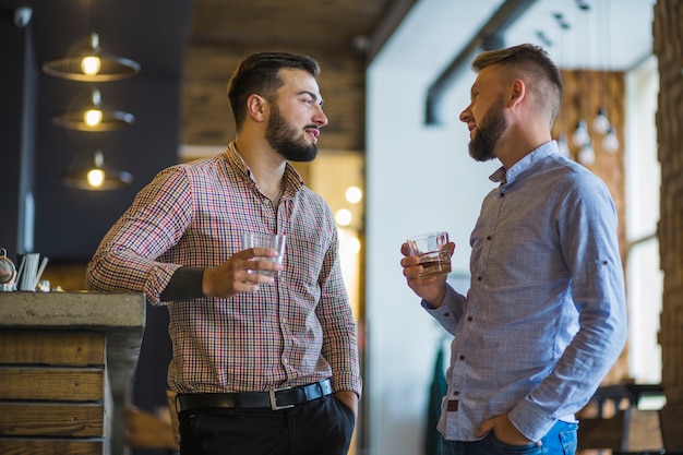 Zwei junge männliche Freunde, die das Glas Getränke stehen am Barzähler halten