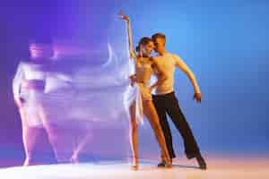 Kostenloses Foto zwei junge professionelle tänzer, die isoliert über blauer und violetter wand mit farbverlauf trainieren
