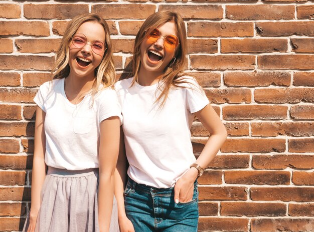 Zwei junge schöne blonde lächelnde Hippie-Mädchen im weißen T-Shirt des modischen Sommers kleidet. . Positive Models, die Spaß an Sonnenbrillen haben