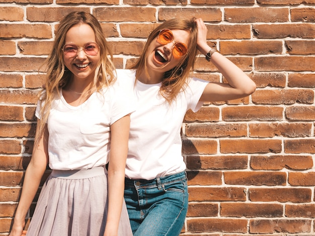 Zwei junge schöne blonde lächelnde hippie-mädchen im weißen t-shirt des modischen sommers kleidet. . positive models, die spaß an sonnenbrillen haben