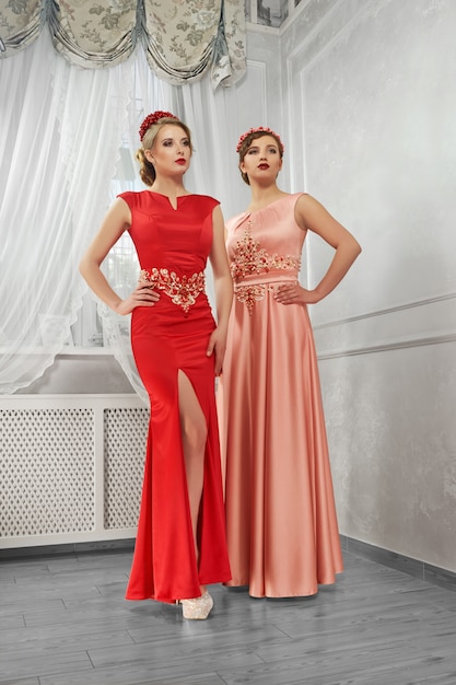 Zwei junge, schöne Frauen in langen, abendroten und pfirsichfarbenen Kleidern