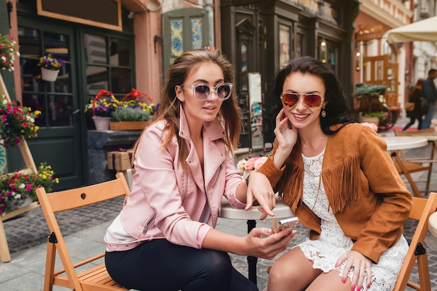 Zwei junge schöne Hipsterfrauen, die am Café sitzen