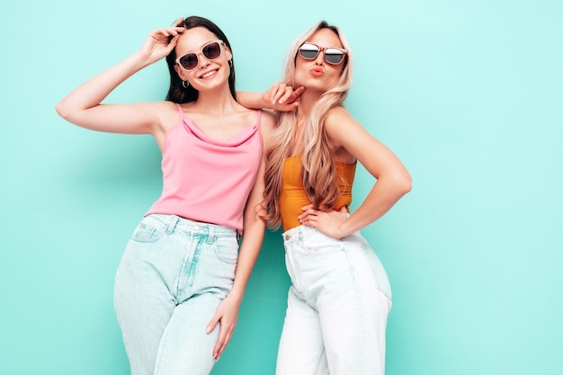 Zwei junge schöne lächelnde brünette Hipster-Frauen in trendiger Sommerkleidung Sexy sorglose Frauen posieren in der Nähe der blauen Wand Positive Models, die Spaß haben Fröhlich und glücklich