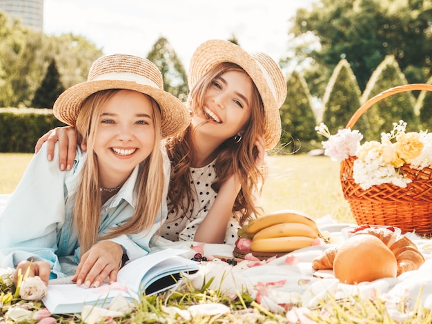 Zwei junge schöne lächelnde frauen in trendigem sommerkleid und hüten. sorglose frauen, die draußen picknick machen.