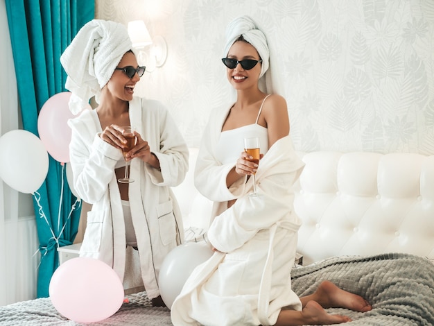 Zwei junge schöne lächelnde Frauen in weißen Bademänteln und Handtüchern auf dem Kopf