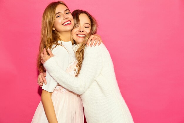 Zwei junge schöne lächelnde Hippie-Frauen in der Weißkleidung des modischen Sommers. Sexy sorglose Frauen, die nahe rosa Wand aufwerfen. Positive Models umarmen sich