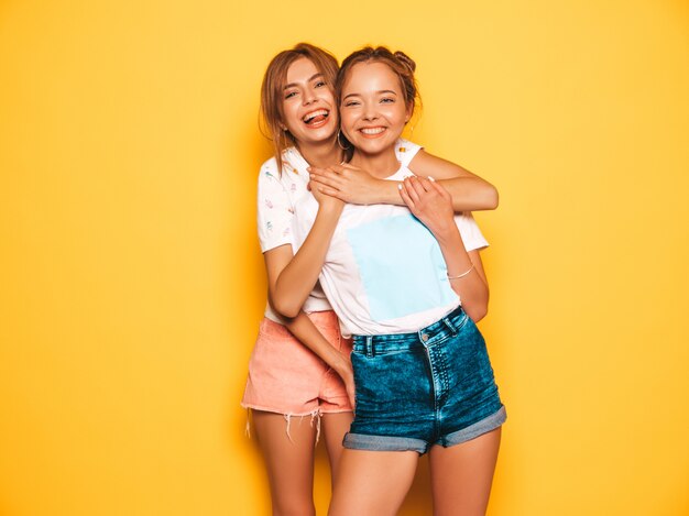 Zwei junge schöne lächelnde Hippie-Mädchen in der modischen Sommerkleidung. Sexy sorglose Frauen, die nahe gelber Wand aufwerfen. Positive Models werden verrückt und haben Spaß