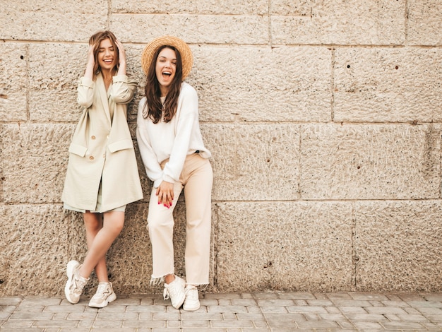 Zwei junge schöne lächelnde Hipster-Frau im trendigen weißen Pullover und Mantel