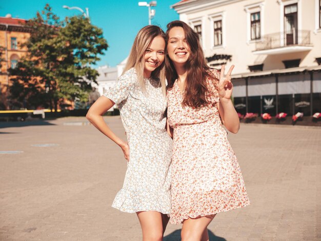 Zwei junge schöne lächelnde Hipster-Frauen in trendigen SommerkleidernSexy sorglose Frauen, die auf der Straße posieren Positive reine Models, die sich bei Sonnenuntergang amüsieren, umarmen und verrückt werden