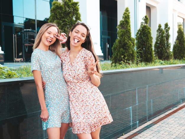Zwei junge schöne lächelnde Hipster-Frauen in trendigen SommerkleidernSexy sorglose Frauen, die auf der Straße posieren Positive reine Models, die sich bei Sonnenuntergang amüsieren, umarmen und verrückt werden