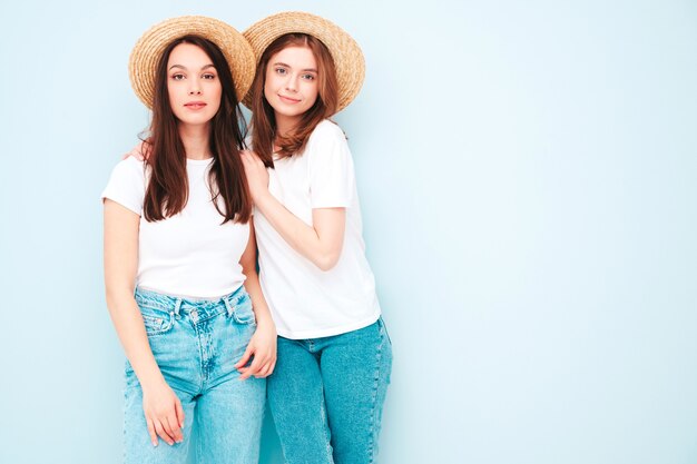 Zwei junge schöne lächelnde Hipster-Frauen in trendigen weißen T-Shirts und Jeanskleidern im gleichen Sommer