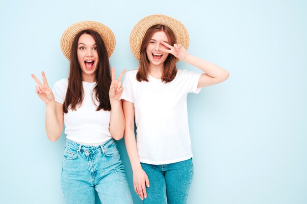 Zwei junge schöne lächelnde Hipster-Frauen in trendigen weißen T-Shirts und Jeanskleidern im gleichen Sommer