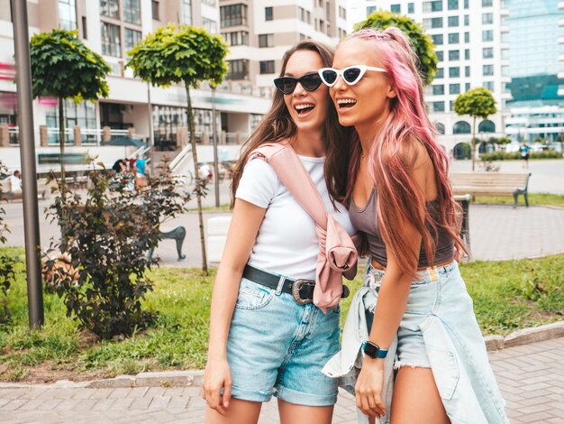 Zwei junge, schöne, lächelnde Hipster-Frauen in trendiger Sommerkleidung. Sexy sorglose Frauen, die mit rosa Haaren auf der Straße posieren. Positive reine Models, die sich bei Sonnenuntergang amüsieren. Fröhlich und glücklich