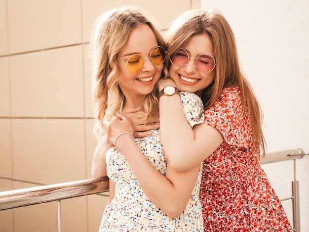 Zwei junge schöne lächelnde hipster-mädchen im trendigen sommer-sommerkleid. sexy sorglose frauen, die auf straßenhintergrund in der sonnenbrille aufwerfen. positive models, die spaß haben und sich umarmen