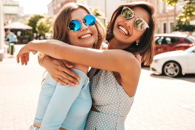 Zwei junge schöne lächelnde hipster-mädchen in der trendigen sommerkleidung. sexy sorglose frauen, die auf straßenhintergrund in der sonnenbrille aufwerfen. positive models, die spaß haben und sich umarmen