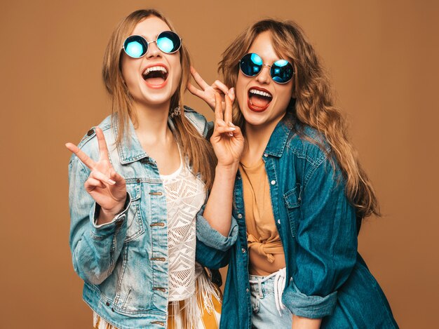 Zwei junge schöne lächelnde Mädchen in der zufälligen Kleidung und in der Sonnenbrille des modischen Sommers. Sexy sorglose Frauenaufstellung. Fotografieren mit der Retro-Kamera