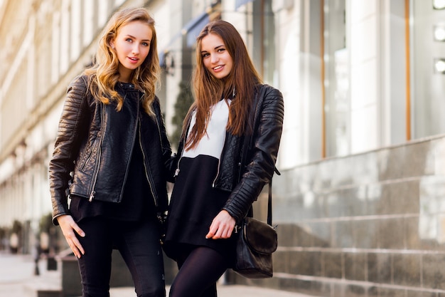 Zwei junge schöne Mädchen, die draußen zusammen aufwerfen. Lifestyle urbane Stimmung. Zentrum Stadthintergrund. Beste Freunde, die schwarzes lässiges Herbstoutfit tragen.