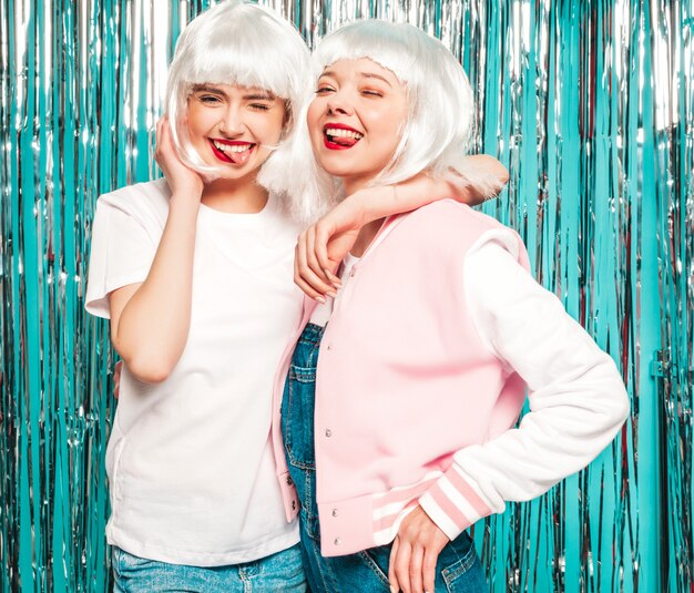 Zwei junge sexy lächelnde Hipster-Mädchen in weißen Perücken und roten Lippen. Schöne trendige Frauen in Sommerkleidung. Sie zeigen Zungen